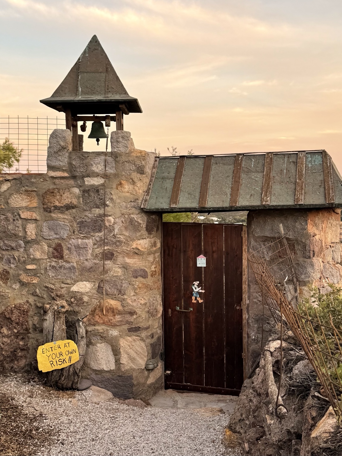 The stone entrance gate and bell, with the yellow Enter at your own risk sign
