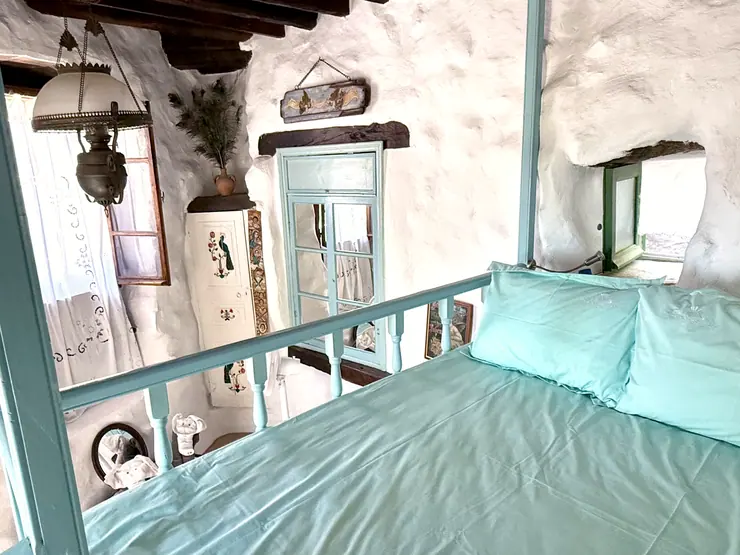 Green bed frame beneath a timber ceiling in a stone bedroom at Eco House Patmos