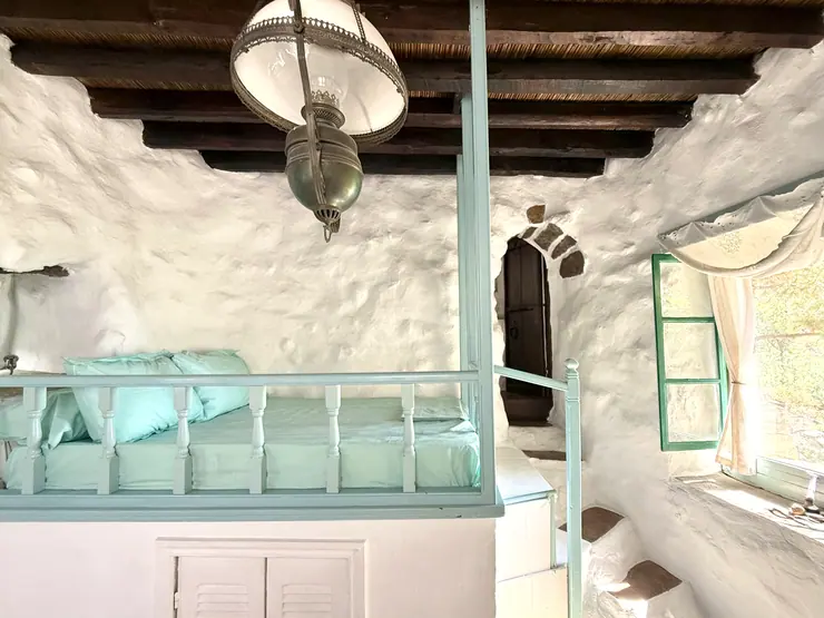 Green bed frame and white stone walls beneath a timber ceiling at Eco House Patmos