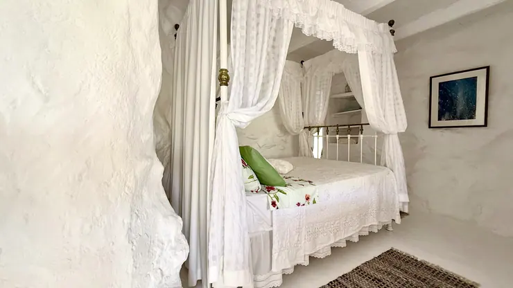 Queen bed with white canopy curtains in a stone-walled bedroom at Eco House Patmos