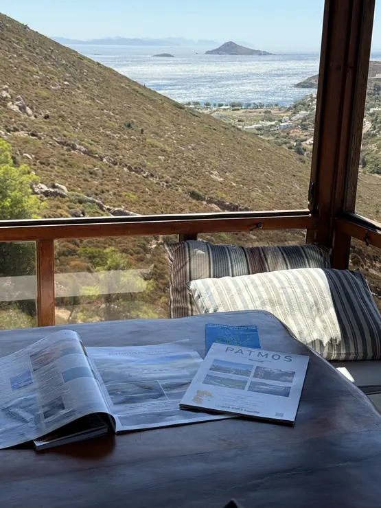 Book on a table beside a sea-view window in the main house at Eco House Patmos