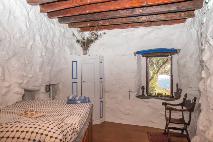 Eco House Patmos – bedroom with stone walls, timber ceiling and a sea-view window