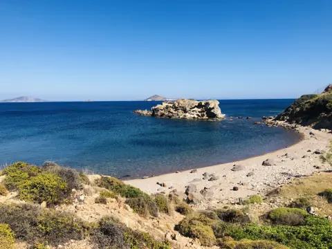 Quiet beach beside blue water and a small rocky islet on Patmos